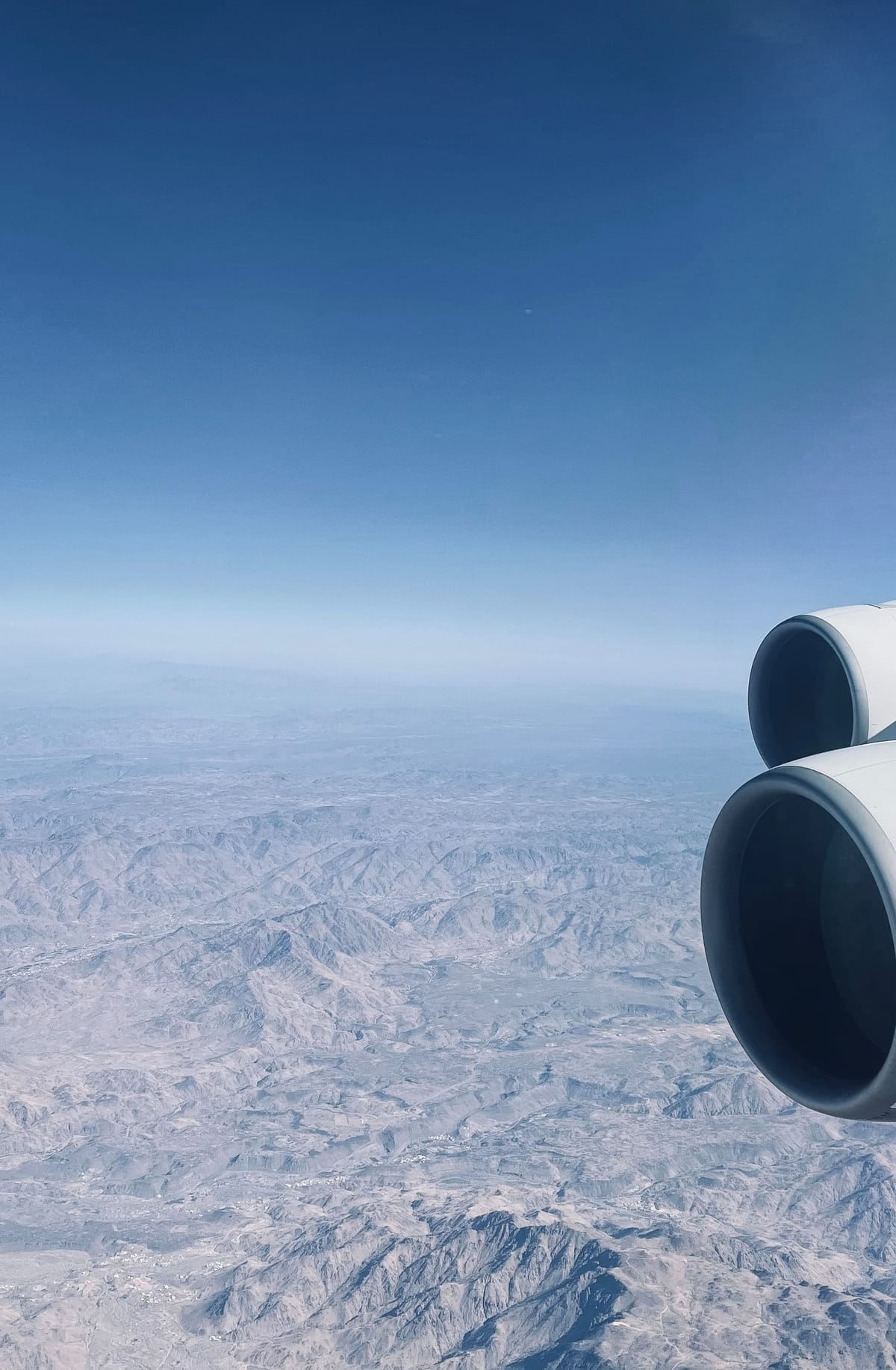 The engines of an airliner over a range of bare mountains, seen from the cabin window