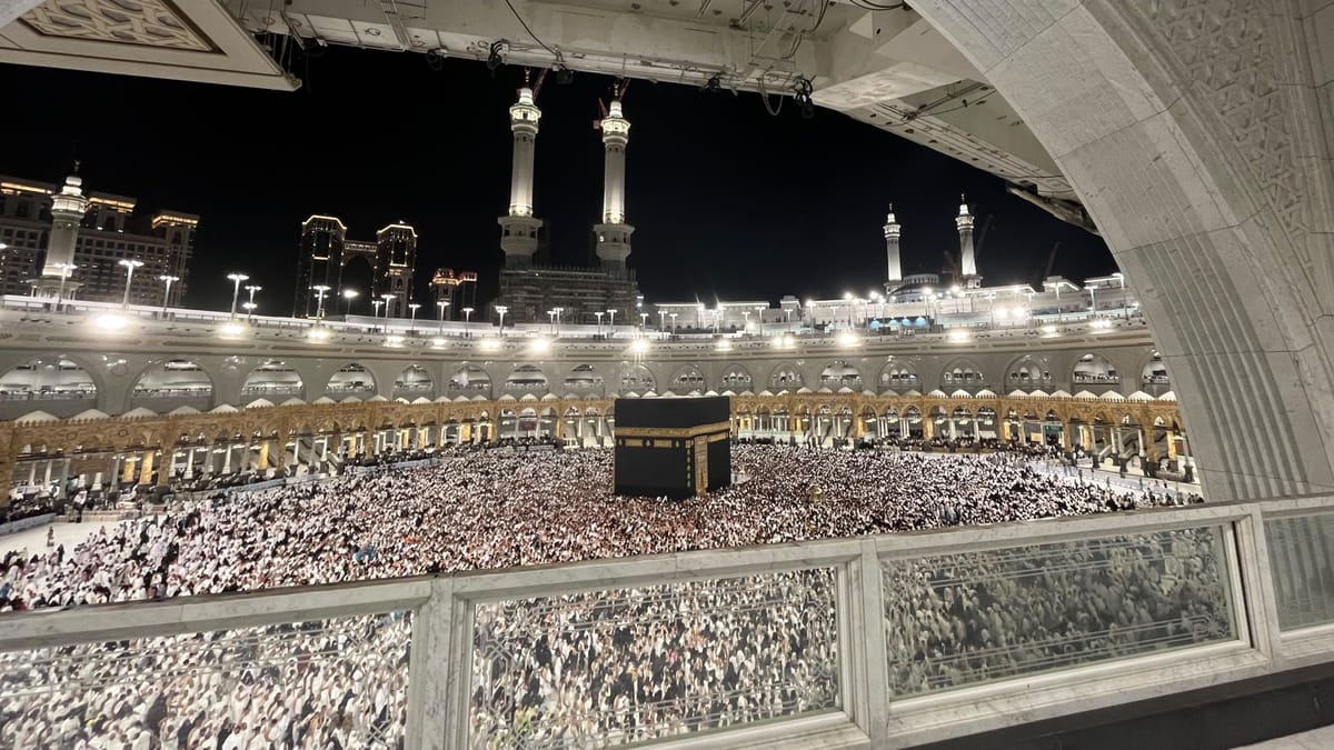 The Kaaba at the centre of Masjid al-Haram at night, the courtyard filled with pilgrims and the minarets lit beyond
