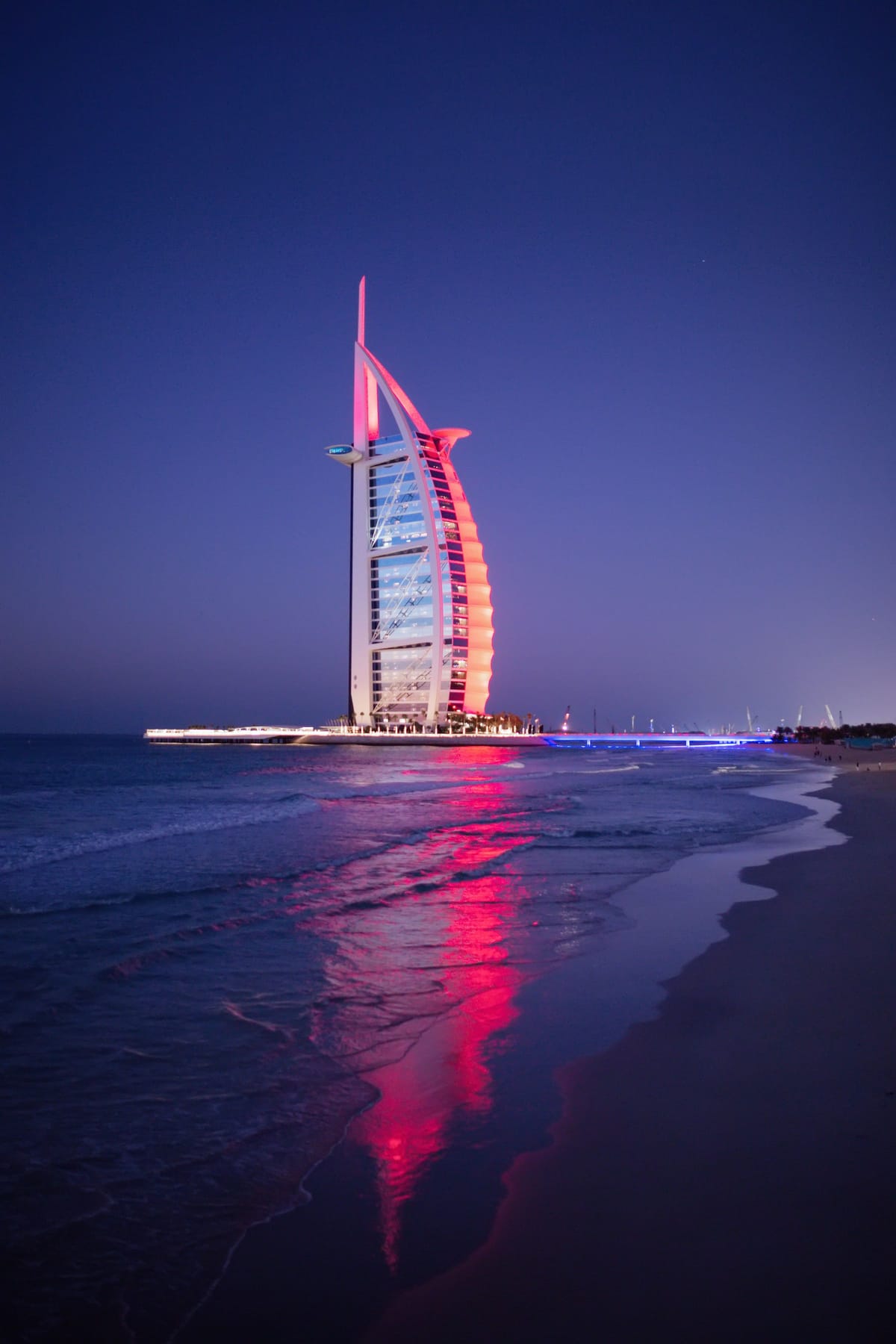The Burj Al Arab lit at dusk on its island off Jumeirah beach, its colours running across the water